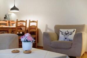 Uma sala de estar com mesa, cadeiras, sofá, luminária e almofada decorativa.