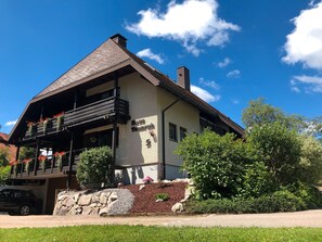 A two-story building with a balcony, a stone wall, and a clear sky. - Ferienwohnung 2 mit Balkon – barrierefrei, 2 Schlafzimmer, Küche, Bernau im Schwarzwald (Bernau im Schwarzwald)
