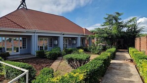 A two-story house with a red-tiled roof, a covered porch, and a well-maintained garden with various shrubs and a pathway. - Blissful lily lodge (Salima)
