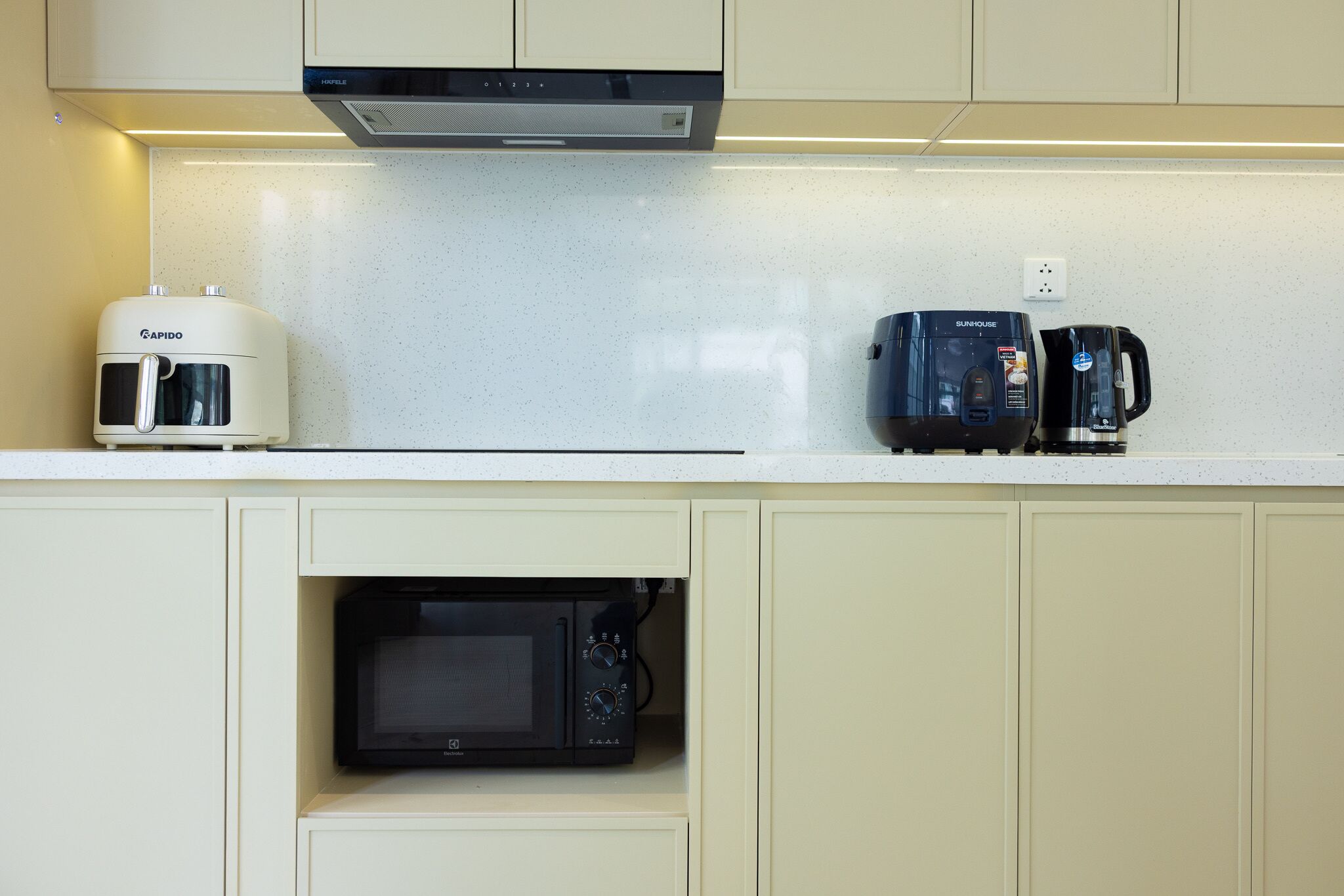 Une cuisine avec un plan de travail blanc, une machine à café, un four à micro-ondes et un grille-pain.