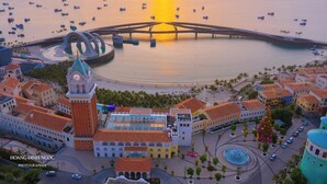 A coastal cityscape with a prominent clock tower, a bridge, and a waterfront promenade.