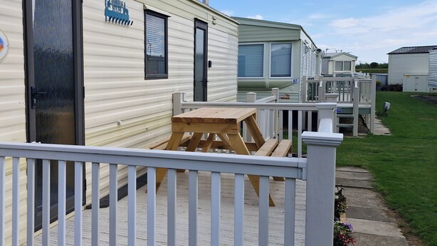 Une rangée de maisons mobiles avec une terrasse en bois et une clôture blanche au premier plan.