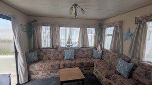 A cozy room with a patterned sofa, a small wooden table, and a ceiling fan. - Seagulls Rest Anderby Creek - Dog Friendly (Skegness)