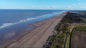 Un paysage côtier avec une plage de sable, un ciel dégagé et une vue lointaine sur une ville ou une agglomération.
