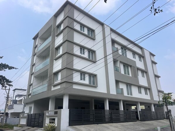 A multi-story residential building with a modern design, featuring balconies and a covered parking area. - Thulasi Avenue (Pollachi)