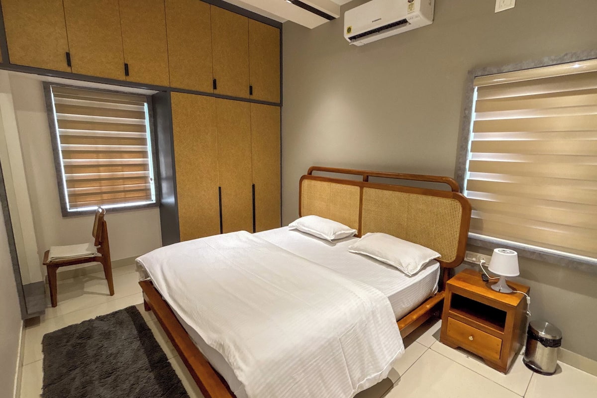 Une chambre à coucher comprenant un lit, une table de chevet, une chaise, une armoire et une fenêtre avec des stores.