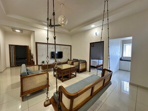 A spacious living room with a large sofa, a dining table, and a television. There is a kitchen area visible through an open doorway. - Thulasi Avenue  (Pollachi)