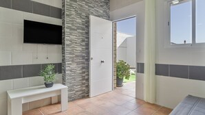 A bathroom with a tiled floor, a bench, a potted plant, a flat-screen TV, and a door leading to an outdoor area.