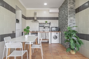 A compact kitchen with a washing machine, a microwave, and a small dining area with chairs and a table.