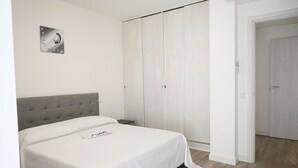 Ein Schlafzimmer mit einem Bett, einem grauen gepolsterten Kopfteil, einem Kleiderschrank und einer Tür zu einem weiteren Raum.