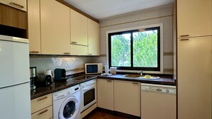 Une cuisine compacte équipée d’un lave-linge, d’un four à micro-ondes, d’une machine à café et d’une fenêtre donnant sur un espace verdoyant.