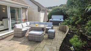 Un patio al aire libre con mobiliario de mimbre, un jacuzzi y un área de estar con paredes de vidrio.