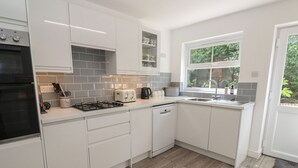 Cocina moderna con armarios blancos, estufa a gas, tostadora y ventana con vista a follaje.