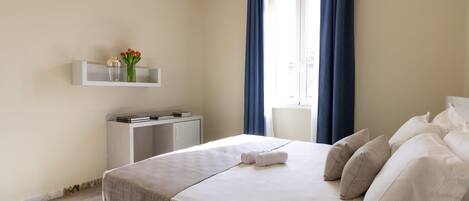 A hotel room with a bed, bedside table, and a window with curtains.