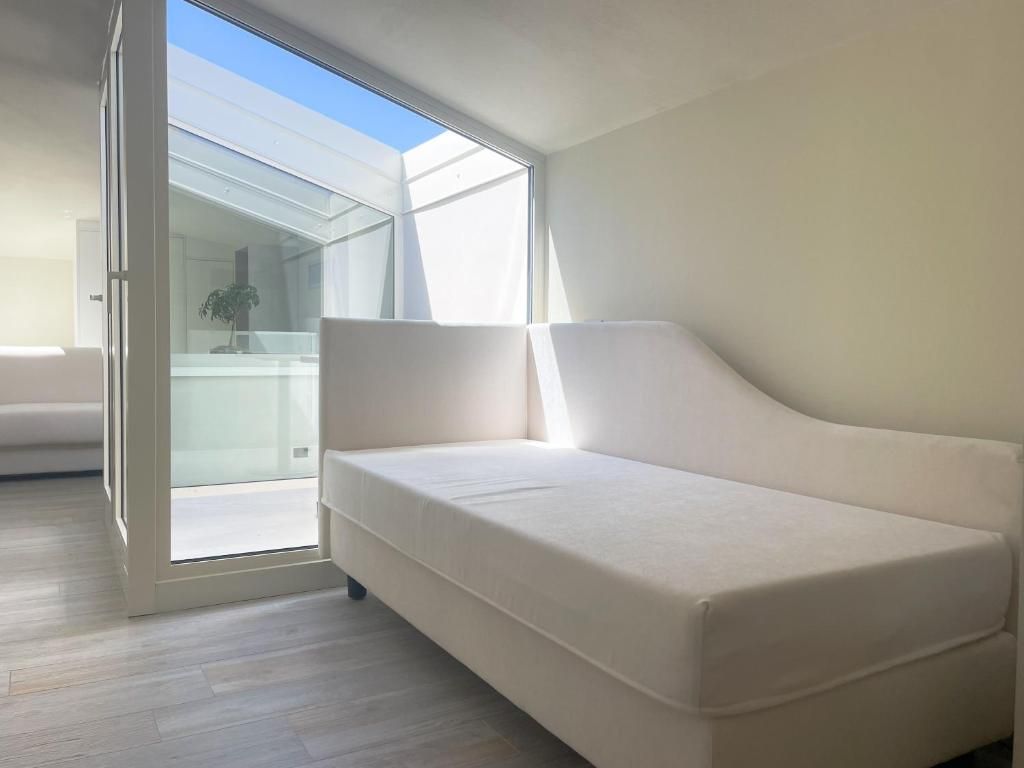 Una habitación moderna con un sofá blanco, un ventanal de vidrio que da a un balcón y suelo de madera.