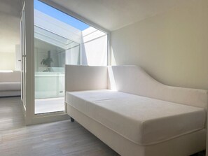 Una habitación moderna con un sofá blanco, un ventanal de vidrio que da a un balcón y suelo de madera.