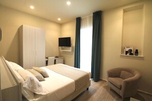 Una camera d'albergo con un letto, una sedia, una televisione, un armadio e una finestra con tende.