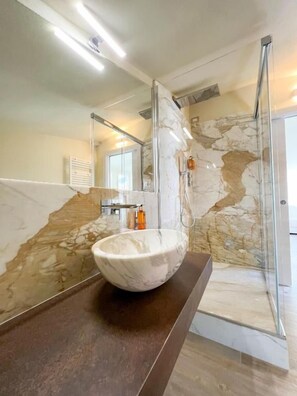 Un bagno con un lavabo in marmo, una cabina doccia in vetro e una parete in marmo.