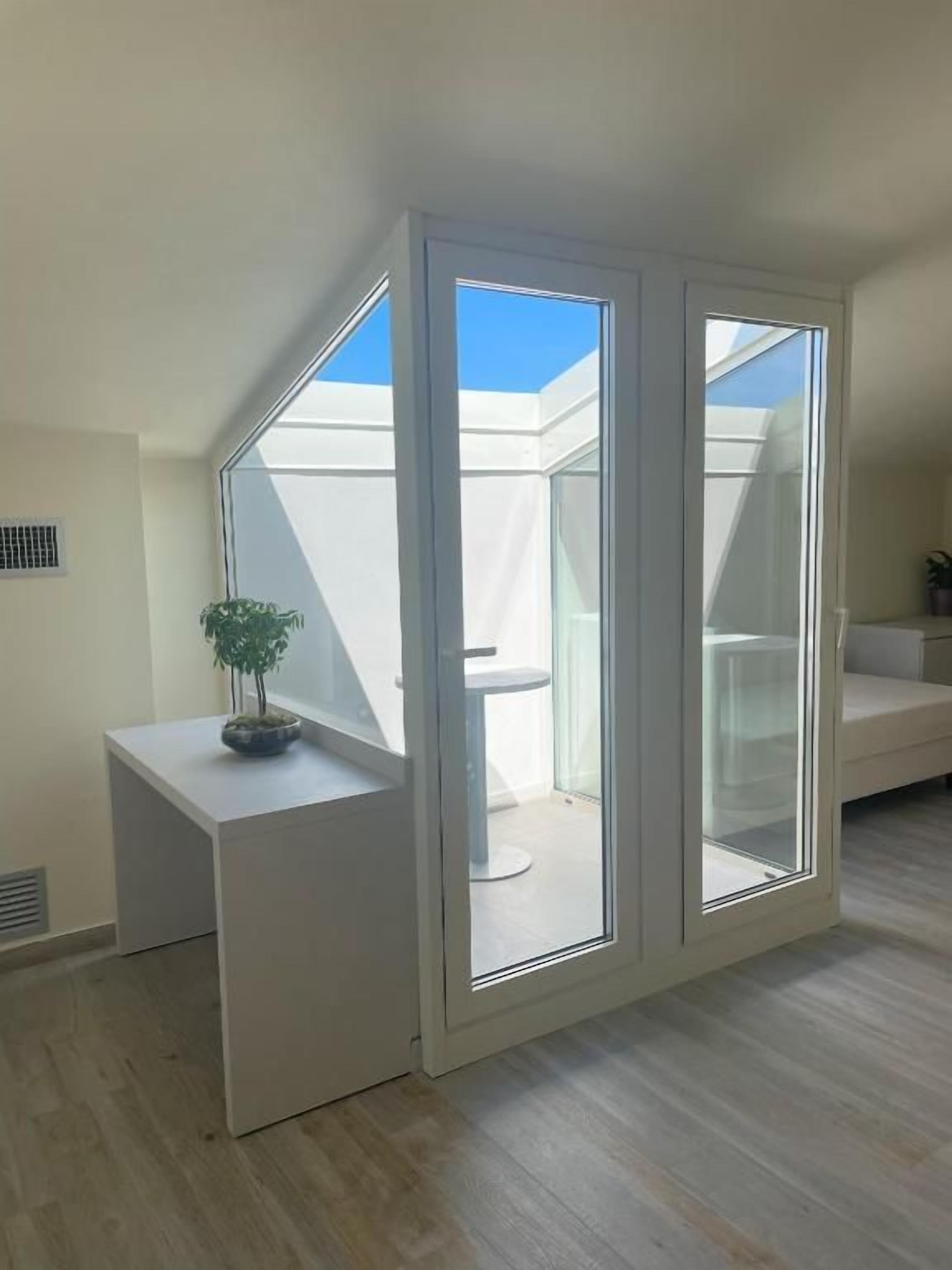 A room with a sliding glass door leading to a balcony, a small white table with a plant, and a white sofa.
