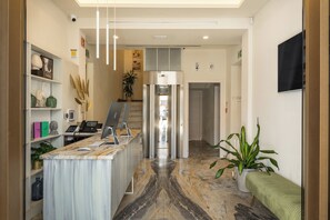 Zona de recepción con mostrador de mármol, una planta y una puerta que da a otra habitación.