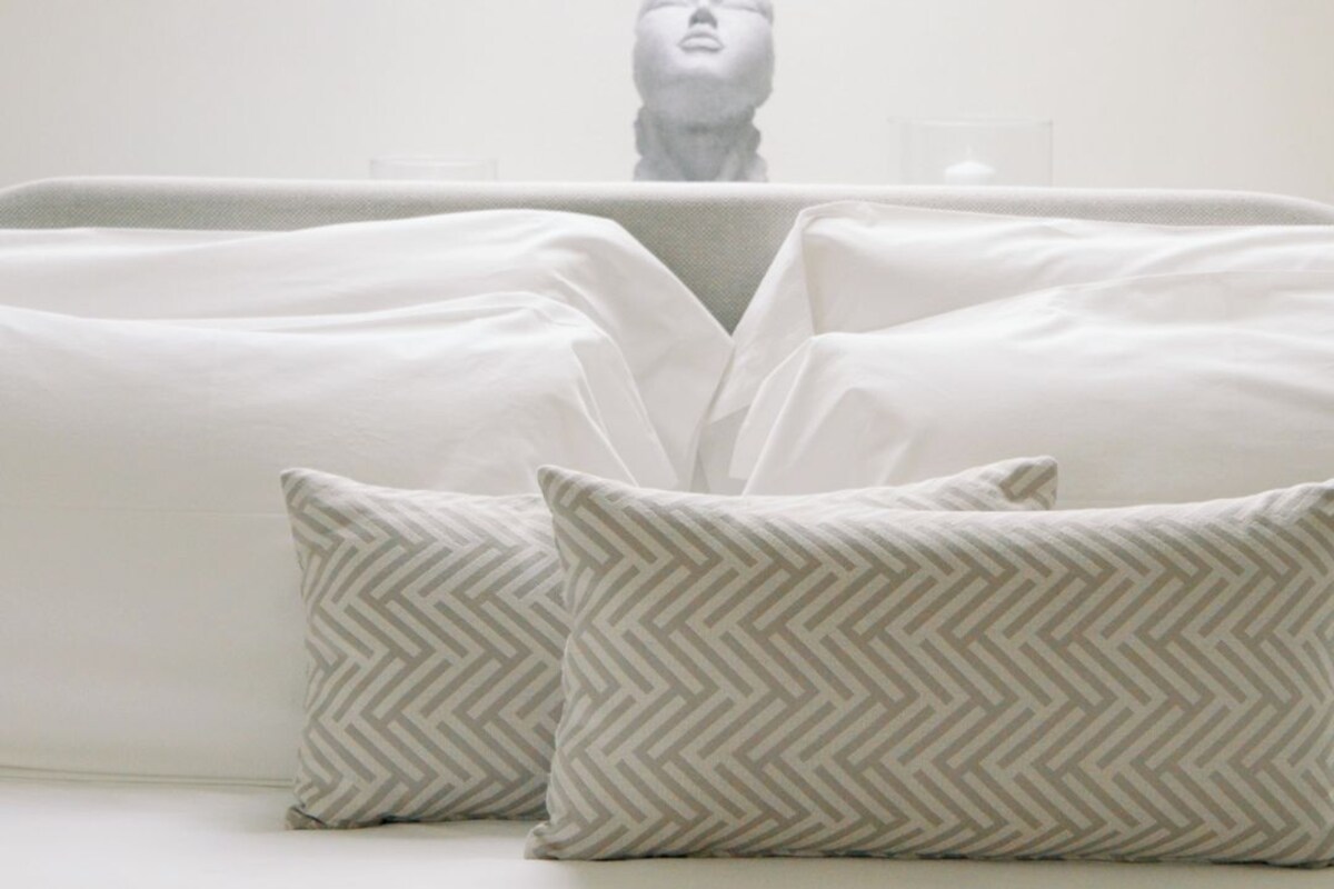 Un dormitorio con tragaluz, una cama con almohadas estampadas y una escultura en la mesita de noche.