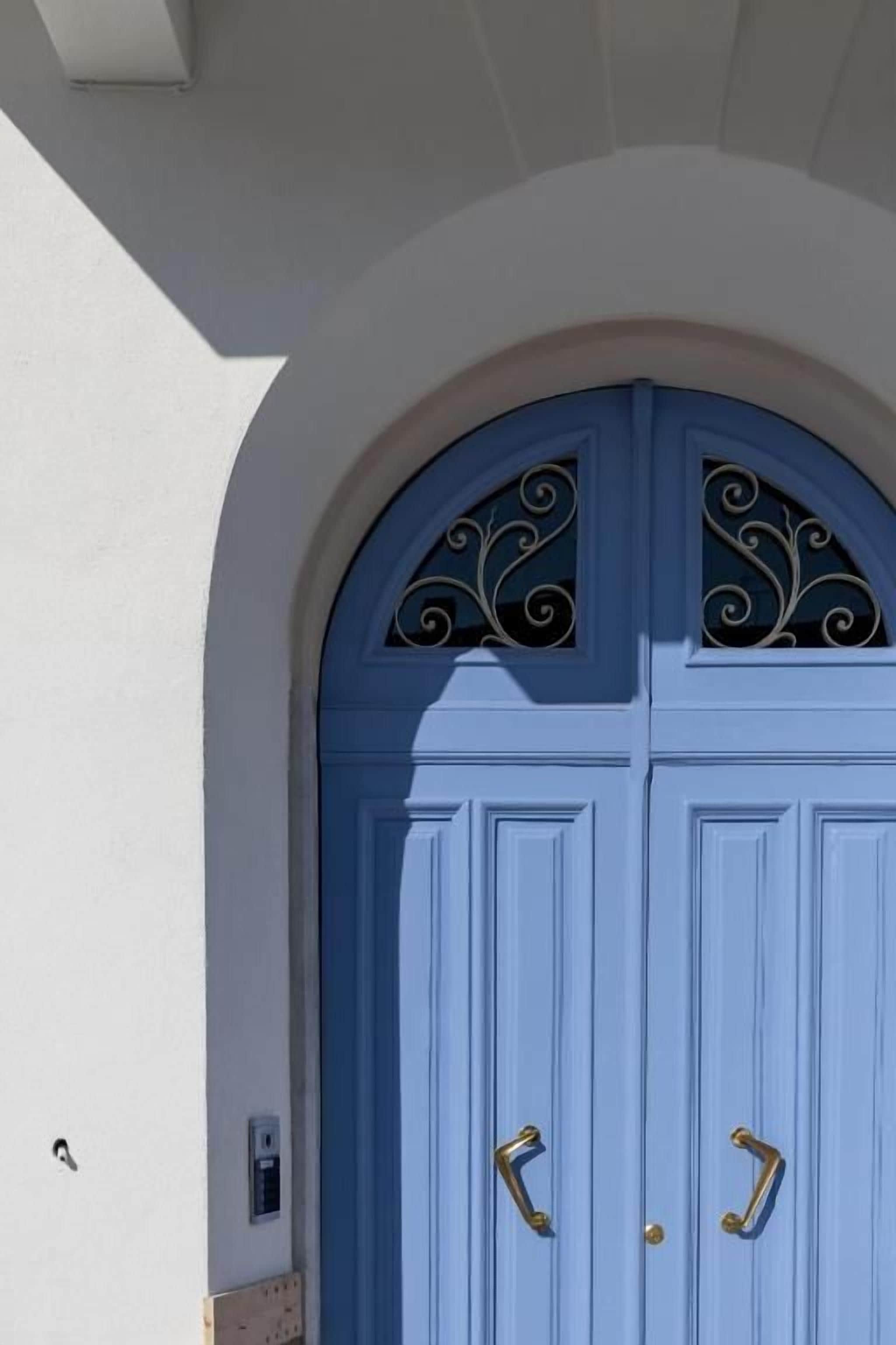 Eine blaue Tür mit verziertem Oberteil und zwei Messinggriffen.