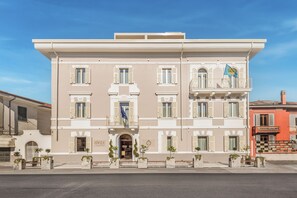 Un hotel de varios pisos con una fachada clásica, una entrada central y una bandera en el balcón.