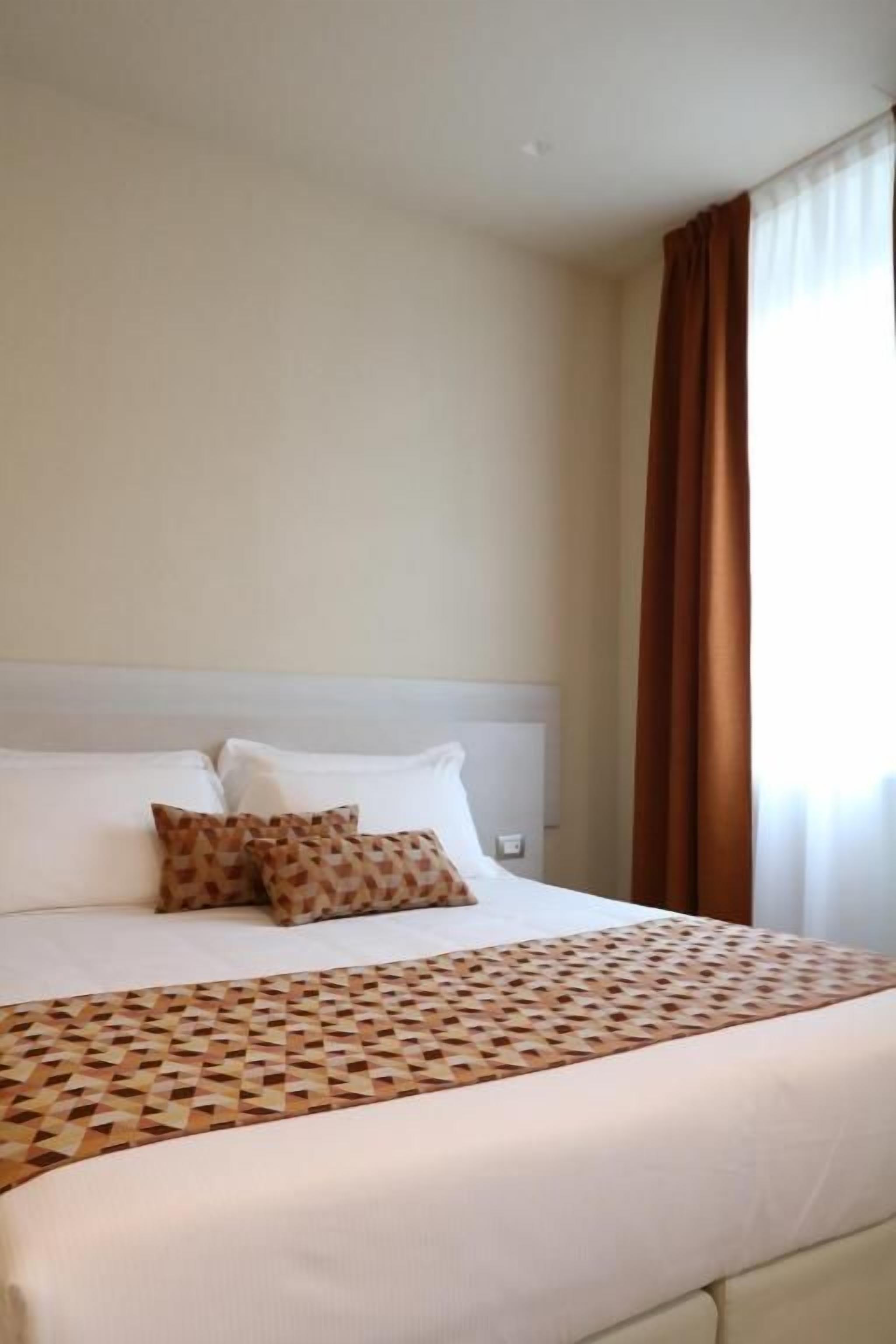 A hotel room with a bed, pillows, and a patterned bedspread.