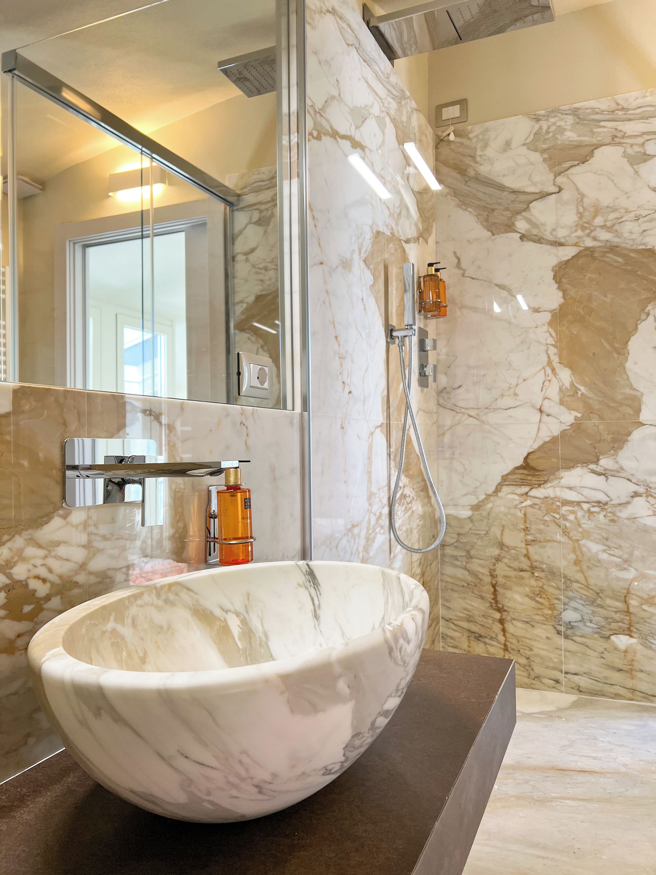 Une salle de bain avec un lavabo en marbre, une douchette à main et un miroir qui reflète une porte.