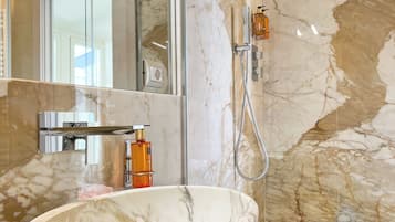 Une salle de bain avec un lavabo en marbre, une douchette à main et un miroir qui reflète une porte.