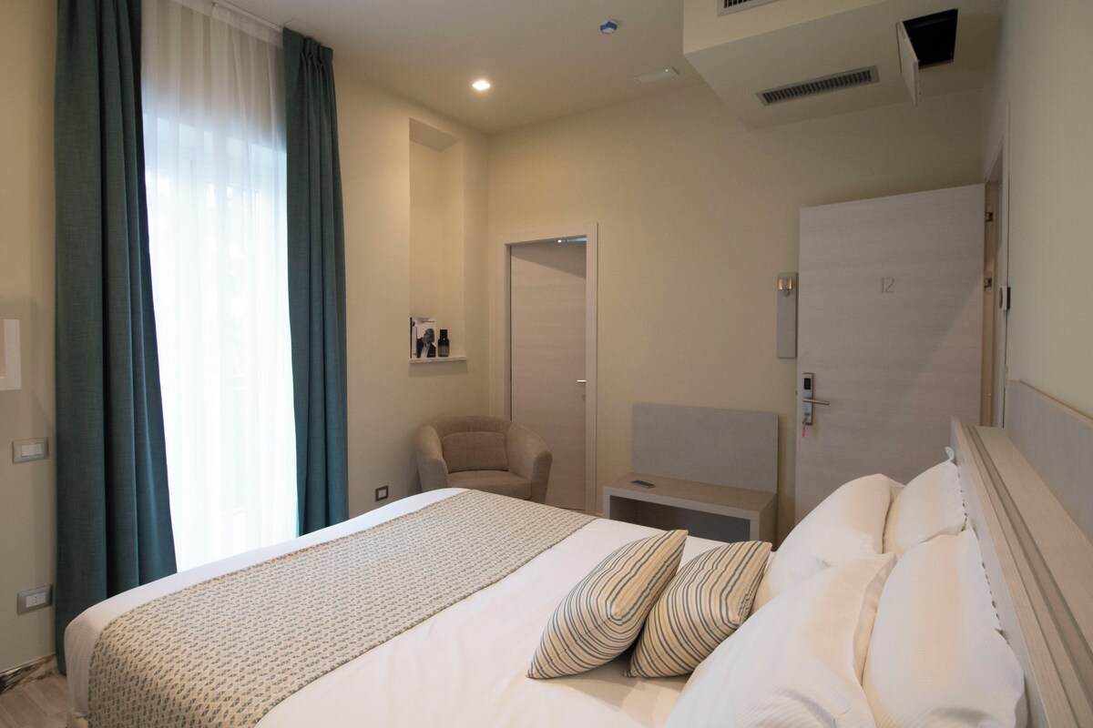 Una habitación de hotel con una cama grande, una mesita de noche, una silla, un armario y un espejo.