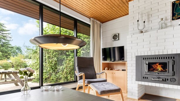 A modern living room with a large window, a fireplace, a television, and a dining area. - "Ognen" - 800m from the sea by Interhome (Væggerløse)