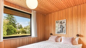 A bedroom with a large bed, wooden walls, a window with curtains, and a painting on the wall. - "Ognen" - 800m from the sea by Interhome (Væggerløse)