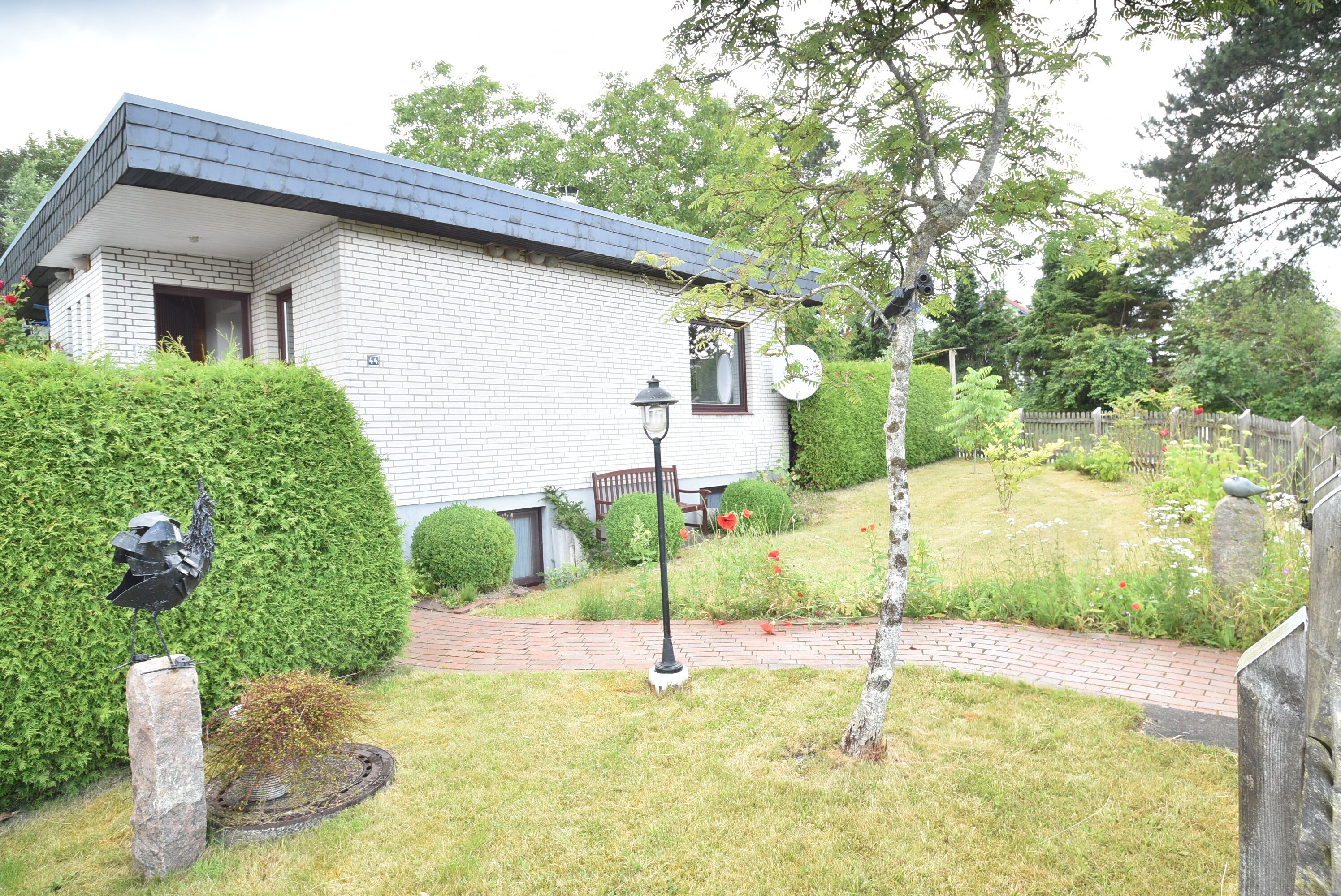 Een modern huis met een bakstenen gevel, een verharde oprit en een verzorgde tuin met heggen en een boom.
