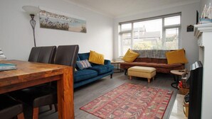 Un salon avec une table à manger en bois, un canapé bleu, un canapé marron et un tapis à motifs.