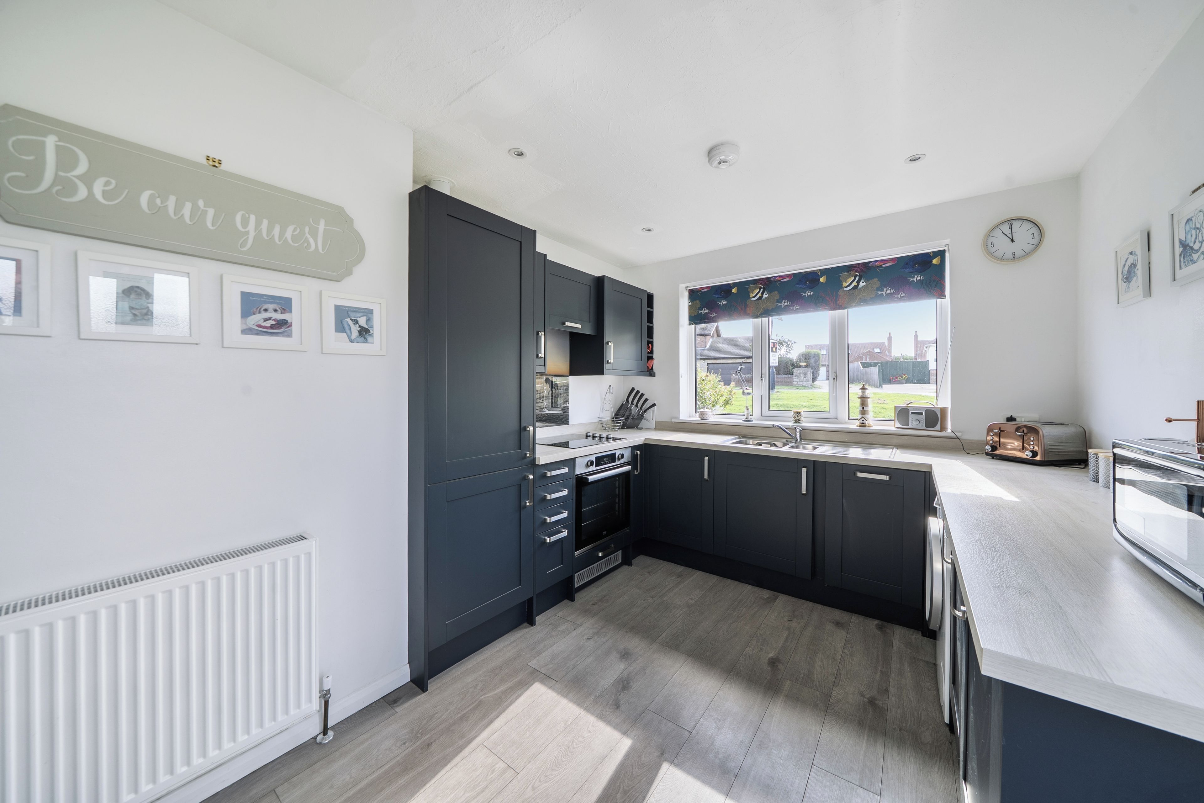 A modern kitchen with dark cabinets, a white countertop, and a window with a view of the outdoors.