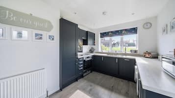 A modern kitchen with dark cabinets, a white countertop, and a window with a view of the outdoors.