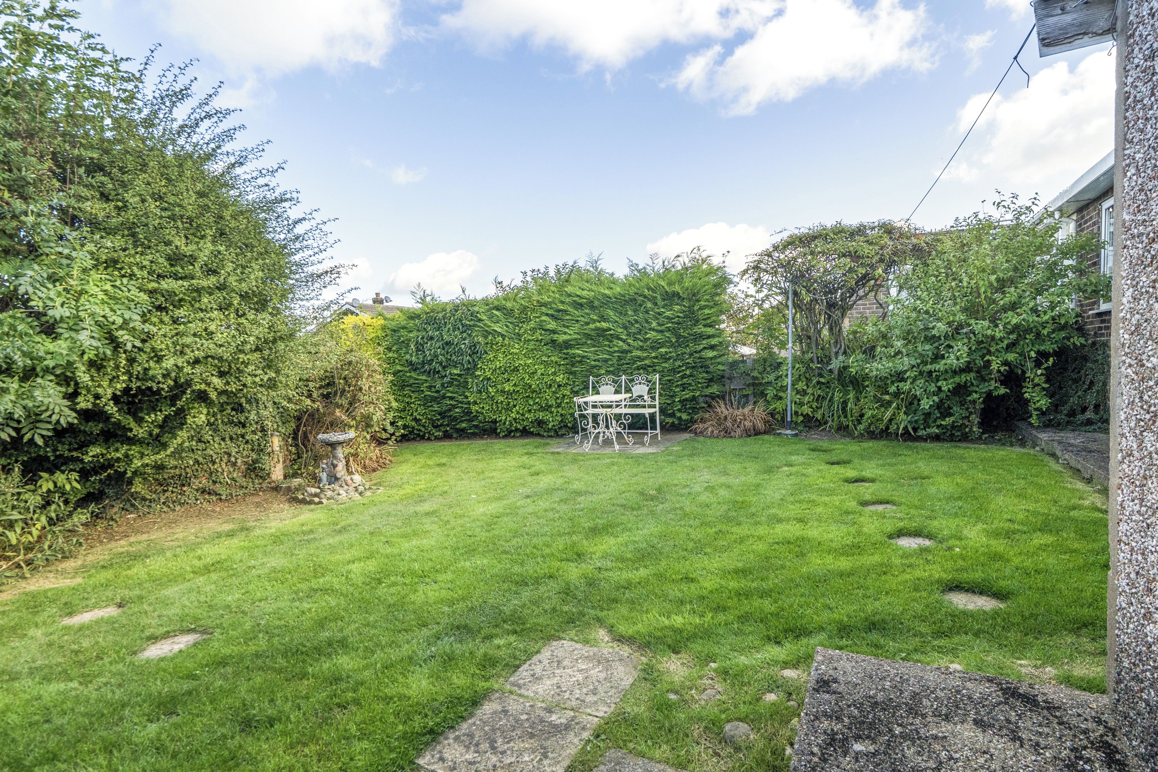 A well-maintained garden with a lawn, a stone pathway, and a metal table with chairs.