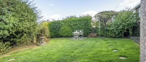 A well-maintained garden with a lawn, a stone pathway, and a metal table with chairs.