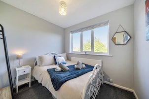 A bedroom with a bed, bedside table, lamp, window, and a wall-mounted mirror.