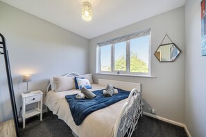 Un dormitorio con cama, mesita de noche, lámpara, ventana y un espejo fijado a la pared.