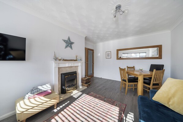Un salon avec une cheminée, une table à manger avec des chaises, un téléviseur fixé au mur et une décoration en forme d’étoile.