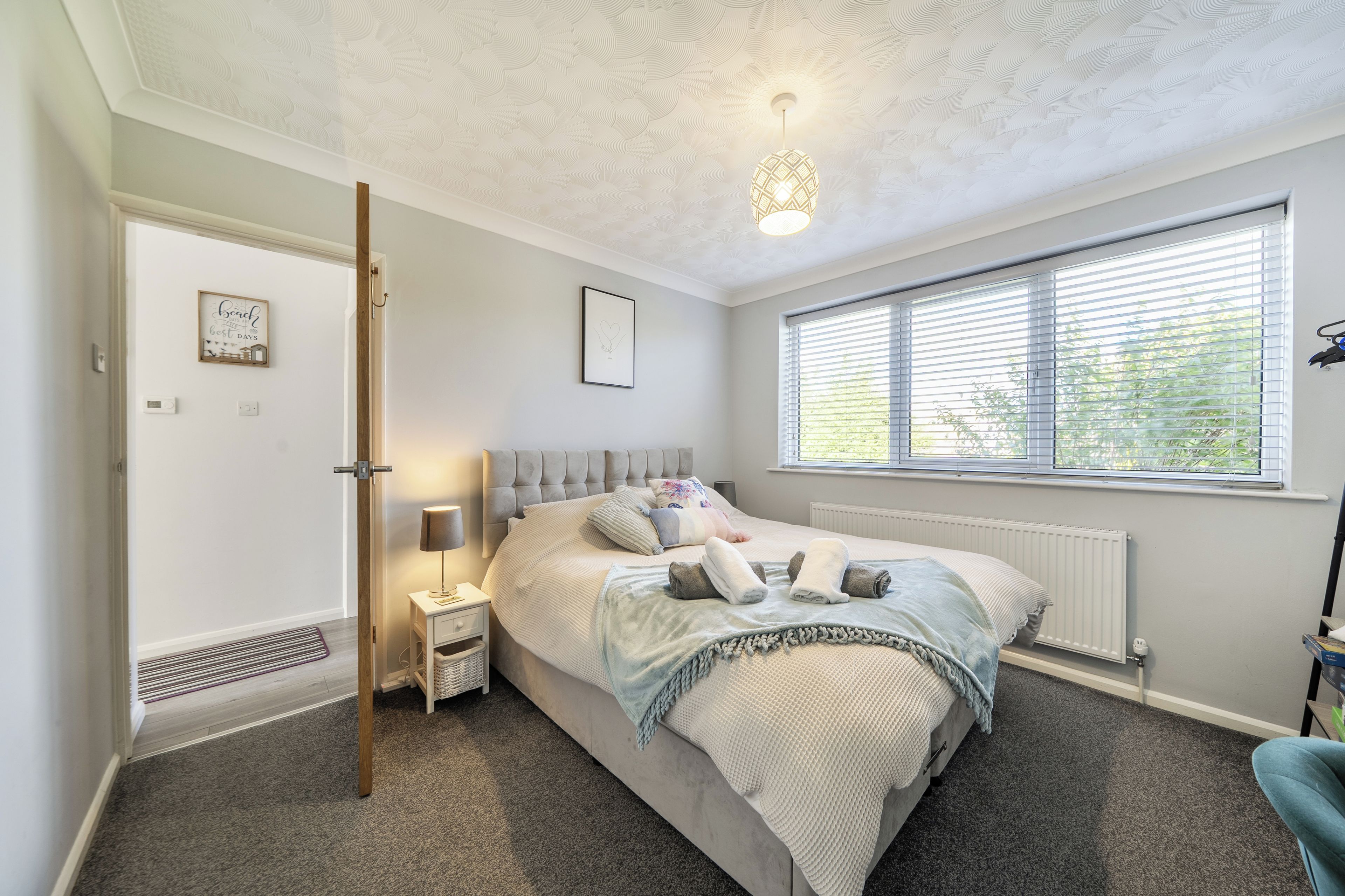 A bedroom with a bed, bedside table, lamp, window, radiator, and a door.