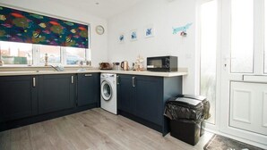 Une cuisine compacte avec des meubles sombres, un lave-linge, un four à micro-ondes et une fenêtre ornée d’une fresque colorée représentant des poissons.