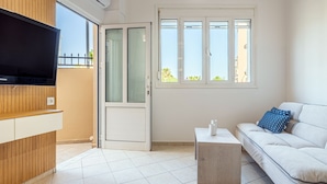 Una sala de estar moderna con una televisión de pantalla plana, un sofá, una mesa de centro y un ventanal corredizo que da a un espacio exterior.
