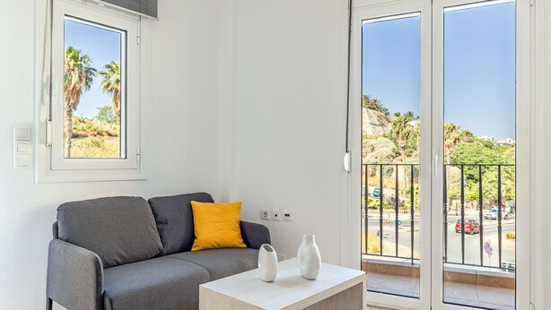 Un salón moderno con un sofá gris, un cojín amarillo y dos jarrones blancos sobre una mesa de madera clara.