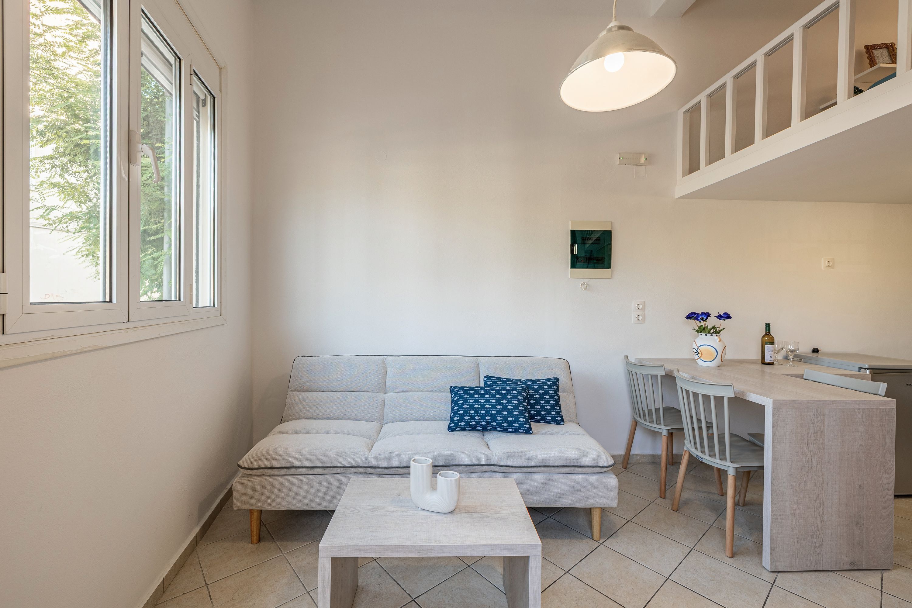 A modern living room with a sofa, a coffee table, and a dining area with chairs and a kitchen counter.