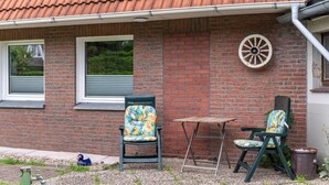 Een bakstenen gebouw met een pannendak, twee stoelen met bloemenstof en een kleine tafel.