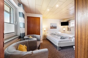 Habitación de hotel con cama, sofá, televisión y ventana con persianas.