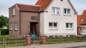 Een huis met twee verdiepingen, gedeeltelijk van baksteen en gedeeltelijk wit, met een houten hek en een duidelijke voordeur.